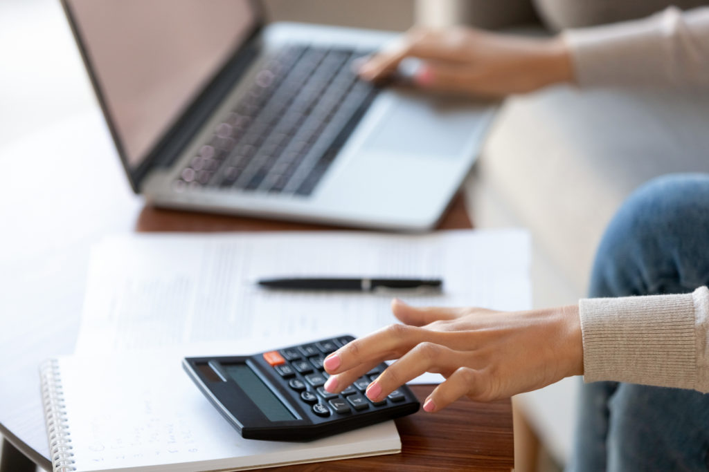 Woman using calculator and laptop for calculating finances.