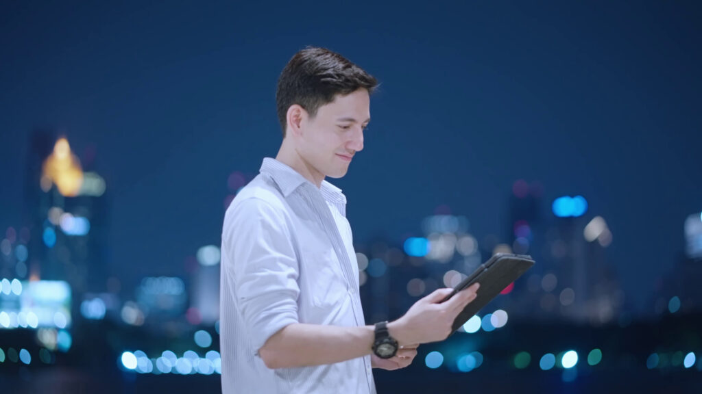 Professional reviewing a tablet at night with a city skyline behind